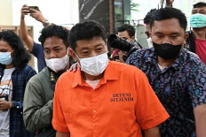 Arrested Japanese national Mitsuhiro Taniguchi (center) is escorted by Indonesian officers prior to a press conference at an immigration office in Jakarta on June 8, 2022. Indonesian police have arrested a Japanese fugitive accused of swindling more than 7 million USD worth of government coronavirus subsidies meant for small businesses back home, an official said on June 8. 