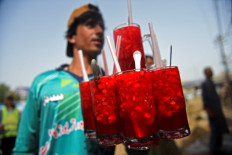 In this photograph taken on May 25, 2022, a vendor prepares to serve Rooh Afza watermelon beverages to customers along a roadside stall in Karachi.