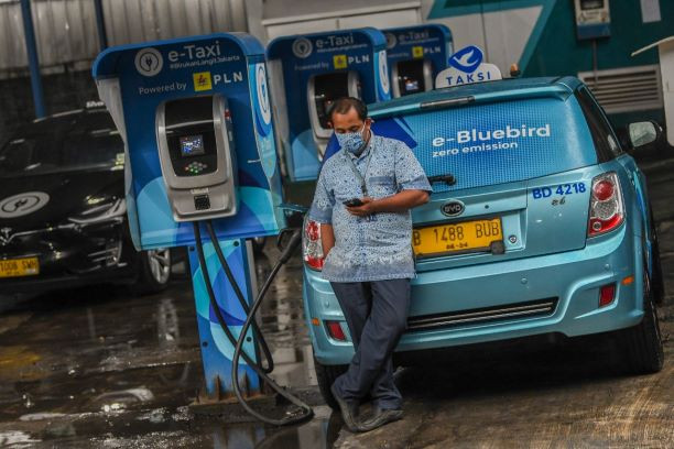 A driver looks at his smartphone July 13, 2022, while waiting for his electric taxi to recharge at Bluebird Group’s Mampang Prapatan pool in South Jakarta.