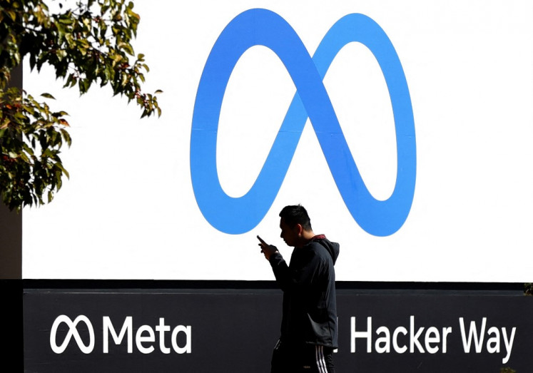 In this file photo taken on October 28, 2021, a pedestrian walks in front of a new logo and the name 'Meta' on the sign in front of Facebook headquarters in Menlo Park, California.