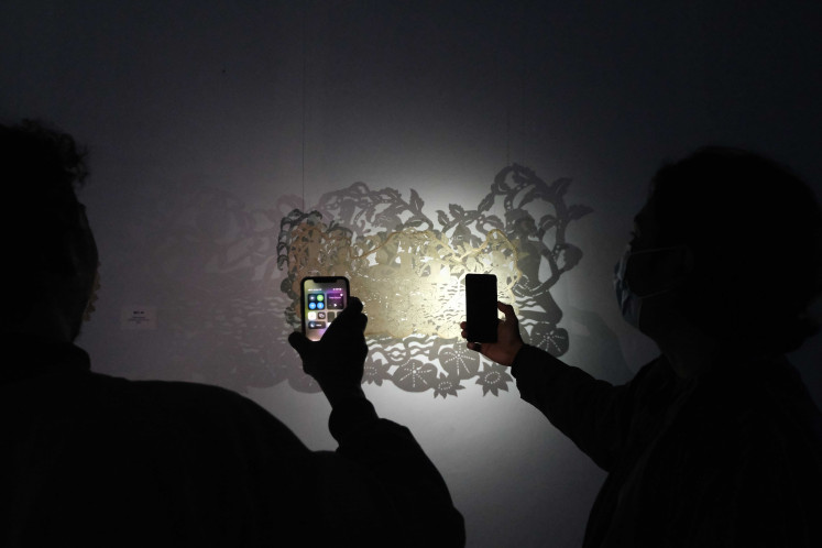 Art Enthusiasts: Exhibition visitors use flashlights on their handheld phones to highlight Gede Sukarya's cowhide carving.  (Courtesy of the Gurat Institute)