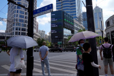 Pedestrians wait to cross a road at a junction near a giant display of stock indexes in Shanghai, China, on Aug. 3, 2022.
