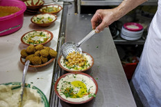 A cook prepares plates of hummus to be served to clients at a restaurant in the Old City of Jerusalem on July 26, 2022.