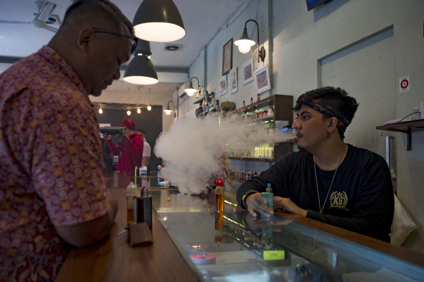 An e-cigarette cafe employee (right) is vaping beside a customer in Jakarta, on Jan. 9, 2018. 