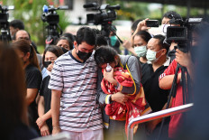 Sittipong Taothawong (left) comforts his wife Kanjana Buakumchan as she holds their child's milk bottle and blanket while standing outside the nursery in Na Klang in Thailand's northeastern Nong Bua Lam Phu province on Oct. 7, 2022, the day after a former police officer killed at least 37 people in a mass shooting at the site. 