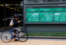 A man on a bicycle stands in front of an electronic board showing stock index quotations from Japan, China and the United States outside a brokerage in Tokyo on Sept. 22, 2022.
