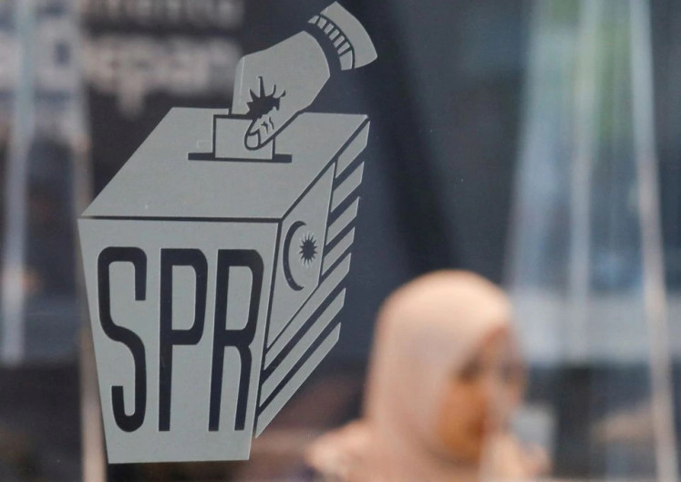 A woman sits behind a window bearing the logo decal of the Election Commission of Malaysia on Oct. 20, 2022, at its headquarters in Putrajaya, the country&rsquo;s administrative center.