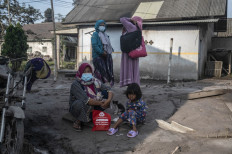 People rest as they salvage their belongings following a volcanic eruption by Mount Semeru at Kajar Kuning village in Lumajang on December 5, 2022. Indonesia's Mount Semeru erupted on December 4 spewing hot ash clouds a mile high and rivers of lava down its side while sparking the evacuation of nearly 2,000 people exactly one year after its last major eruption killed dozens.
