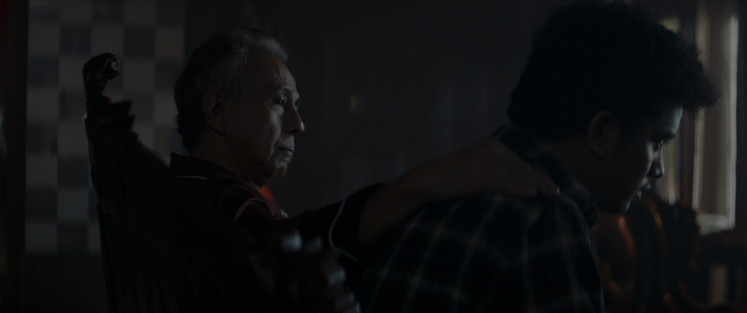 Still image: Purna (Arswendy Bening Swara, left) looks over Rakib (Kevin Ardilova) as the two sit in the darkness of the empty mansion. (Courtesy of KawanKawan Media)