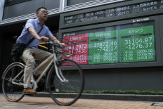 A man cycles past a sign (C) showing the numbers on the Nikkei-225 stock index and the New York Stock Exchange (R) in Tokyo on September 14, 2022, after stocks opened down following a near four percent drop on Wall Street overnight. 