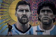 A man passes by a mural depicting Argentine football stars Lionel Messi (left) and late Diego Maradona (right) in the eve of Qatar 2022 World Cup final football match between Argentina and France in Buenos Aires, on December 16, 2022. 
