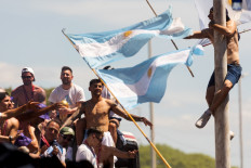 A fan of Argentina clinging to a pole cheers as the team parades on board a bus after winning the Qatar 2022 World Cup tournament, in Buenos Aires province, on December 20, 2022. Millions of ecstatic fans are expected to cheer on their heroes as Argentina's World Cup winners led by captain Lionel Messi began their open-top bus parade of the capital Buenos Aires on Tuesday following their sensational victory over France.
