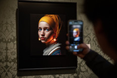 A visitor takes a picture with his mobile phone of an image designed with artificial intelligence by Berlin-based digital creator Julian van Dieken (C) inspired by Johannes Vermeer's painting 'Girl with a Pearl Earring' at the Mauritshuis museum in The Hague on March 9, 2023.