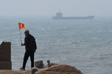 A man walks with a flag as a ship passes by behind him on Pingtan island, the closest point to Taiwan, in China’s southeast Fujian province on April 8, 2023. China launched military drills around Taiwan on April 8, in what it called a “stern warning“ to the self-ruled island's government following a meeting between its president and the US House speaker.

