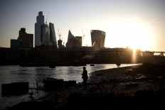 A person stands on the bank of the River Thames during sunrise, with the City of London financial district in the background, on April 4, 2023.