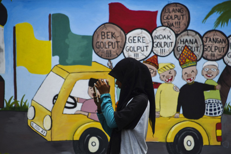 A girl uses her mobile phone in front of an Indonesian election campaign mural ahead of the polls at Banda Aceh, Aceh province, on March 17, 2019. Just like the 2019 election, the young population will again become the majority of voters in the 2024 presidential race.