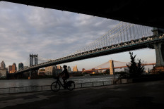 A woman is seen in silhouette riding a bike past the Manhattan Bridge at sunrise in New York City, US, June 3, 2023.