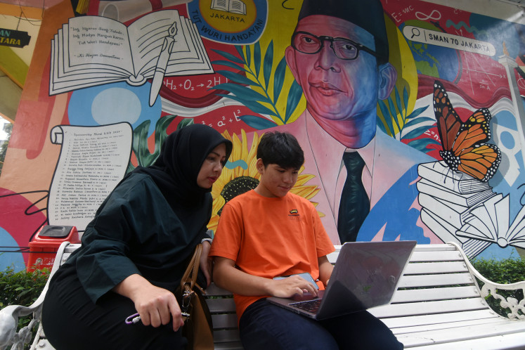 A woman accompanies her son to fill in an online registration form
outside State High School 70, South Jakarta, on June 13, 2023, the first day of enrolment in elementary schools, junior high schools and senior high schools.