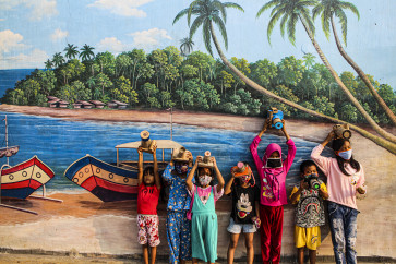Children proudly pose with their cardboard cameras against the backdrop of a coastal village.