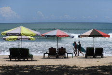 Surfers carry their board past chairs and umbrellas along Kuta Beach near Denpasar, Bali, on March 14, 2023.