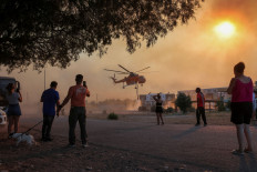 People look at a firefighting helicopter filling water from a pool, as a wildfire burns in the village of Gennadi, on the island of Rhodes, Greece, on July 25, 2023.