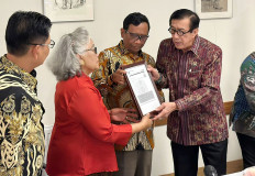 Coordinating Political, Legal and Security Affairs Minister Mahfud MD (second right) and Law and Human Rights Minister Yasonna Laoly (right) give a framed image of a five-year multiple entry visa  on Aug. 27, 2023, to Sri Budiarti (second left), who studied abroad on a government scholarship during Sukarno’s presidency, in Amsterdam. The government has committed to reinstate the rights of victims of past human rights violations, as recommended by a nonjudicial commission on rights abuses.