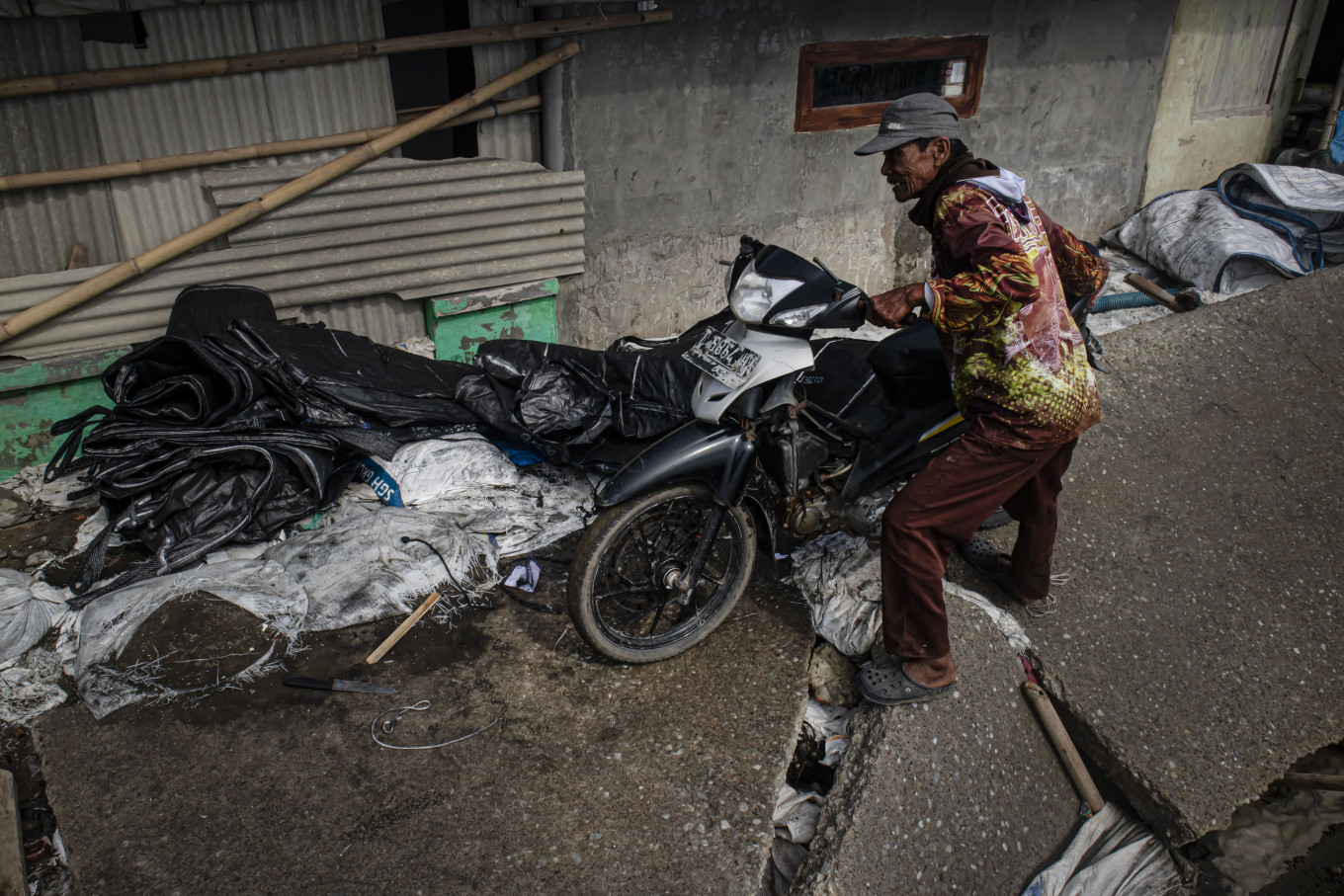 A resident pushes his motorcycle on a damaged road. 