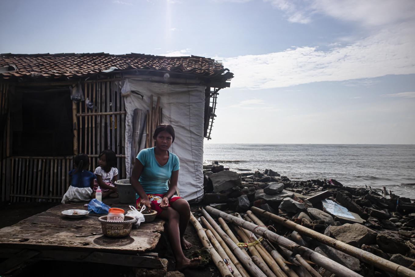 Inyem and her two in front of their house, which is sinking because of coastal erosion. (Portrait)