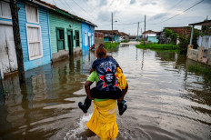A man carries a woman on his back as he wades through the water in a flooded area of Batabano, Mayabeque Province, Cuba, on August 28, 2023, as Tropical Storm Idalia approaches the western tip of the island nation. 