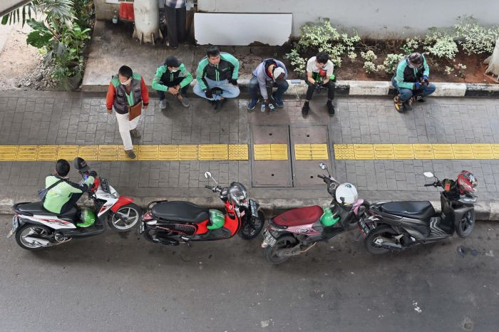 Drivers of on-demand transportation services companies Gojek and Grab wait for orders on June 24, 2020, along a sidewalk in Jakarta.
