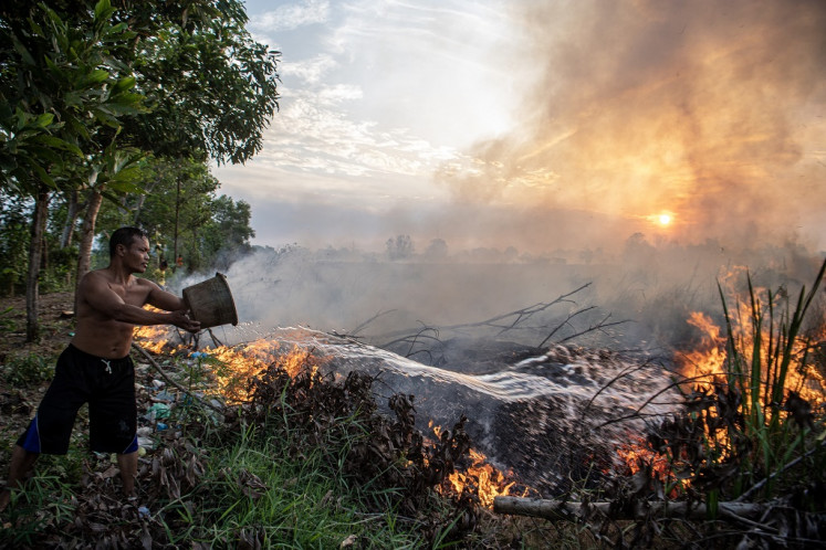 A man throws water in an attempt to douse a wildfire in Pemulutan district, Ogan Ilir regency, South Sumatra, on Sept. 12, 2023.
