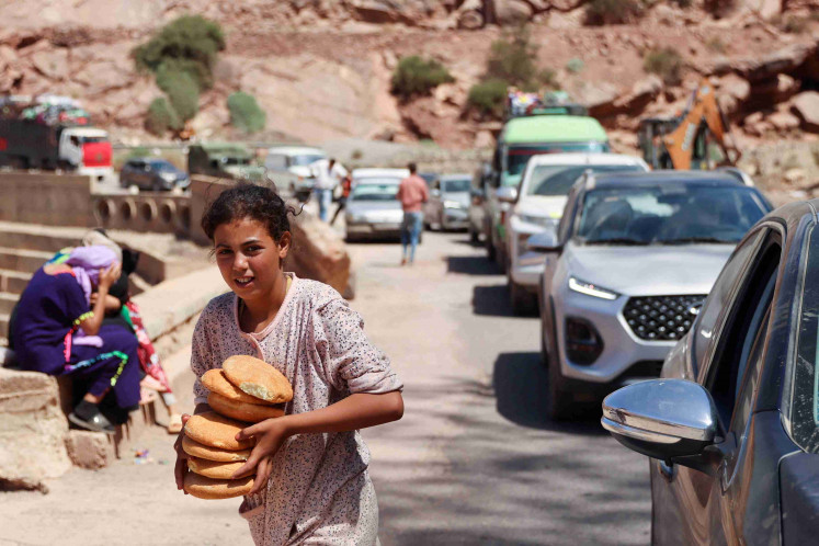 A girl carries bread received from a volunteer as people in vehicles wait for the road to be cleared from debris in the aftermath of a deadly earthquake near the village of Tallat n'Yakoub, Morocco September 12, 2023.