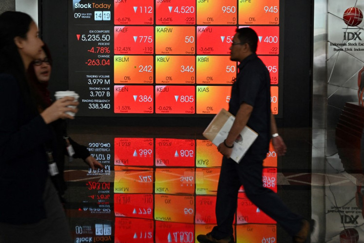 People walk past a screen showing Indonesia Stock Exchange (IDX) prices in Jakarta in March 2020.