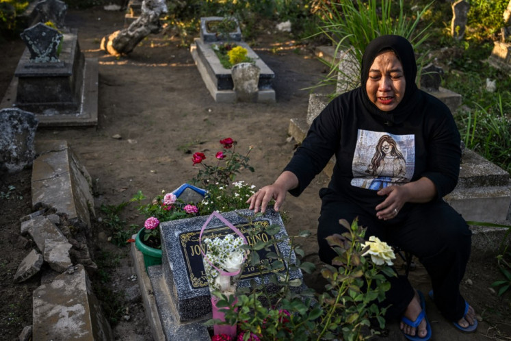 This picture taken on Sept. 21, 2023 shows Cholifatul Nur reacting as she sits beside the grave of her only child Jovan Farellino, who was 15 when he died in the stampede that killed 135 people at the Kanjuruhan football stadium on October 1, 2022, in Malang, East Java. Fifteen-year-old Jovan Farellino was one of dozens of children killed after a match in the East Javan city of Malang that left 135 people dead, many from suffocation or trampling, in one of the worst tragedies in the sport's history.
