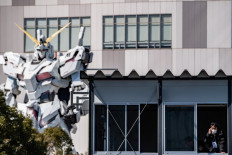 A Gundam statue (left) is placed as an official wearing a facemask looks out as Tokyo 2020 organizing staff climb a wall during a lead climbing test in Tokyo on March 6, 2020. 

