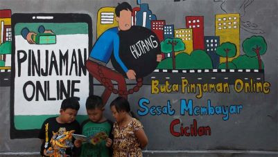 Improving literacy: Children read a book together in front of a mural warning the public of the lure of online lending platforms in the Tempurejo area of Surabaya, East Java, on Sept. 7, 2021. 