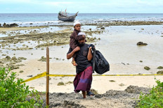 A Rohingya refugee man carries a child as they leave the beach for their tents at Balohan ferry port in Sabang island, Aceh province on December 3, 2023.