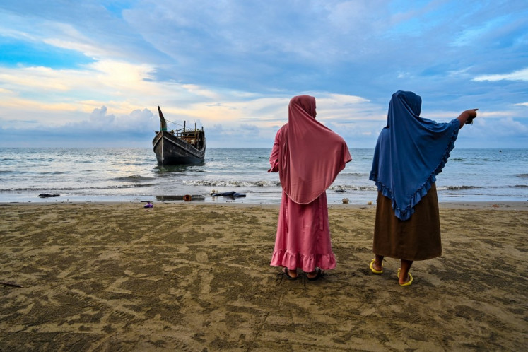 Two women gaze out at sea from the shore on Dec. 10, 2023, near the boat that carried more than 300 Rohingya refugees, the largest group since 2015, to Laweueng Beach in Pidie district, Aceh.