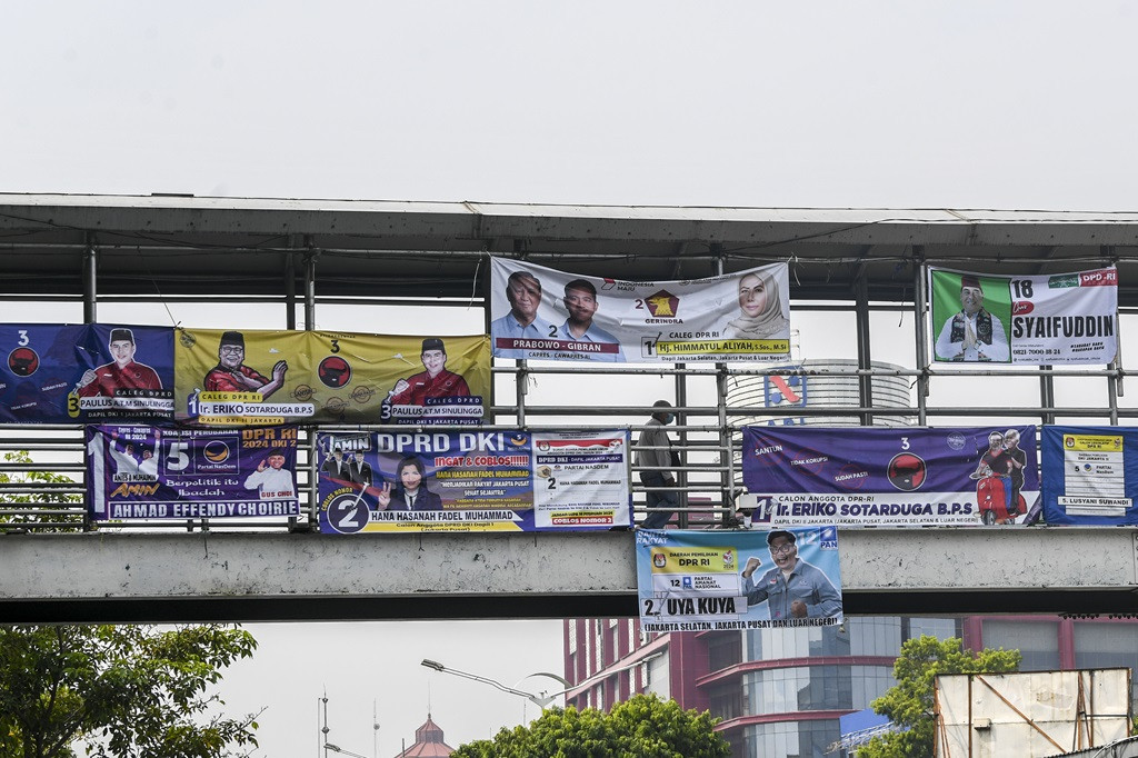 A pedestrian walks through a pedestrian bridge covered by election campaign banners in Salemba, Jakarta on Dec. 7, 2023. 