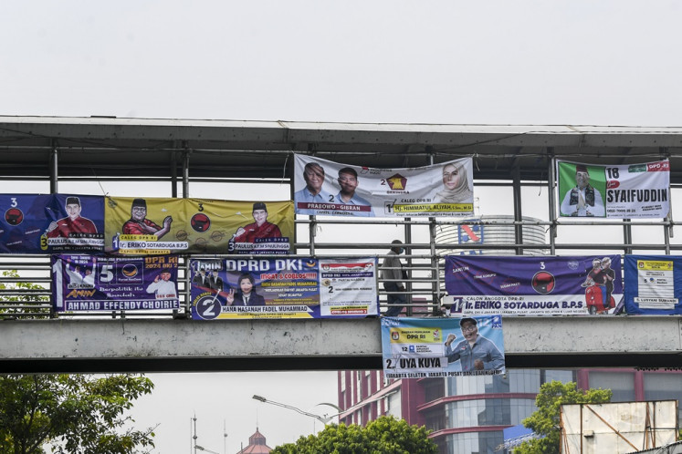 A pedestrian walks through a pedestrian bridge covered by election campaign banners in Salemba, Jakarta on Dec. 7, 2023. 