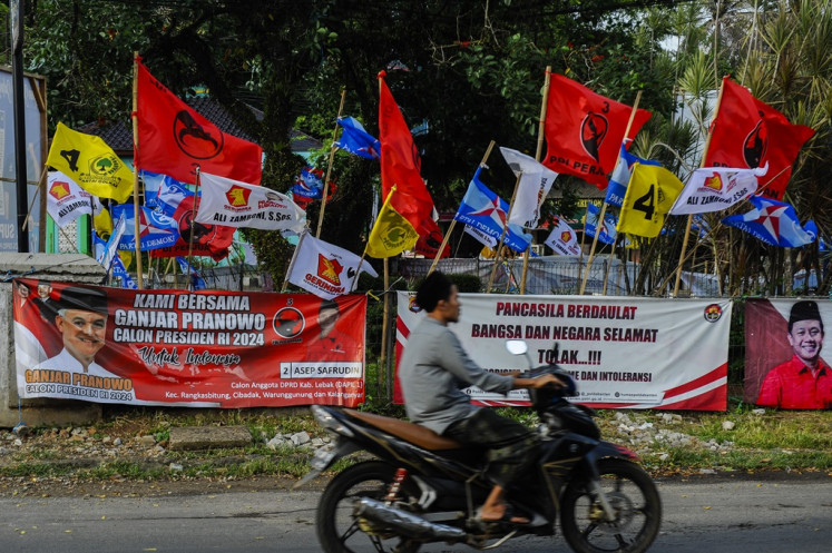 A man rides a motorcycle on Dec. 11, 2023 past a fence covered with a display of colorful campaign banners in Lebak regency, Banten. The General Elections Commission (KPU) has banned the placement of campaign banners in public spaces, including parks and pedestrian bridges.