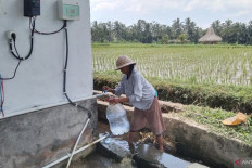 Clean energy: A farmer refills an empty water container on Sept. 2, 2023, with water from a community well in Keliki village, Gianyar regency, Bali. The well uses a pump that runs on energy from a solar power plant, which was provided by state oil and gas giant Pertamina to support Indonesia’s transition to clean energy.
