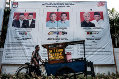 A street food vendor passes by a poster of the three pairs of presidential and vice presidential candidates in Jakarta on Dec. 20, 2023.