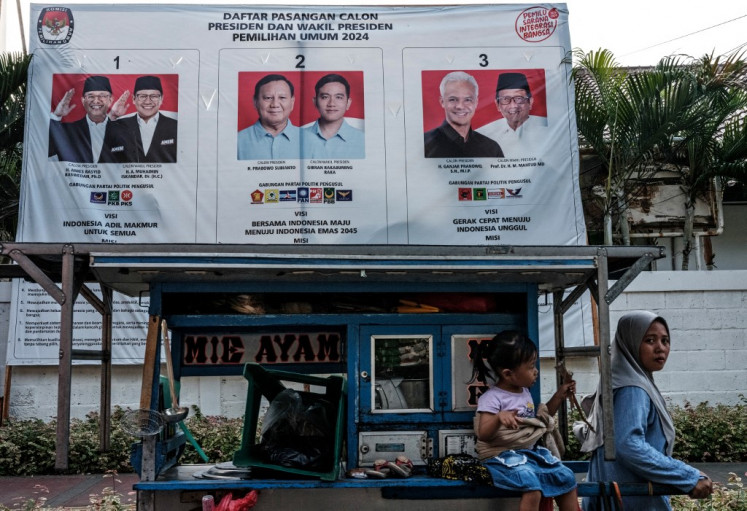 A street food vendor passes by a poster of the three pairs of presidential and vice presidential candidates on Dec. 20, 2023, in Jakarta, ahead of the 2024 general election voting day, slated for Feb. 14, 2024.