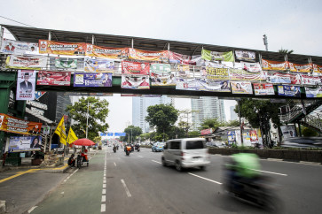 Motorized vehicles pass under a pedestrian bridge that has been completely covered by 2024 election banners, as the campaigning season approaches its second month in Jakarta on Dec. 27, 2023.