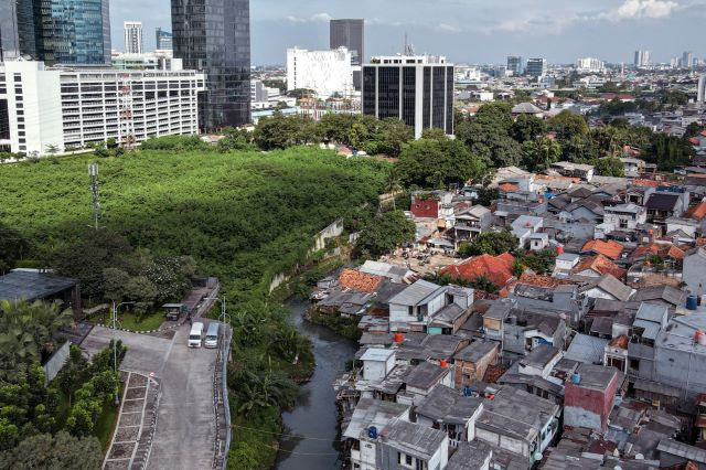 A small river bisects an area in Jakarta, with modern high-rises and a green space on one side and a densely populated neighborhood on the other, in this aerial photograph taken on May 21, 2022.
