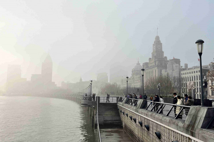 People stand on the Bund as buildings along the Huangpu river are seen shrouded in fog, amid a red alert for heavy fog in Shanghai, China, on Dec. 29, 2023. REUTERS/Xihao Jiang