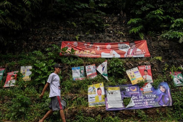 A pedestrian passes near election campaign banners put up on a wall in Setu district, South Tangerang, Banten, on Dec. 29, 2023.