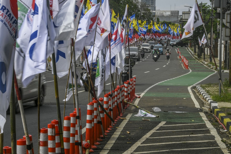 Motorists drive past party flags placed on bicycle lane barriers in Menteng, Jakarta, on Jan. 8, 2024. Some election campaign materials have been put up in places prohibited by local authorities, such as flyovers and highways, harming motorists and pedestrians alike.
