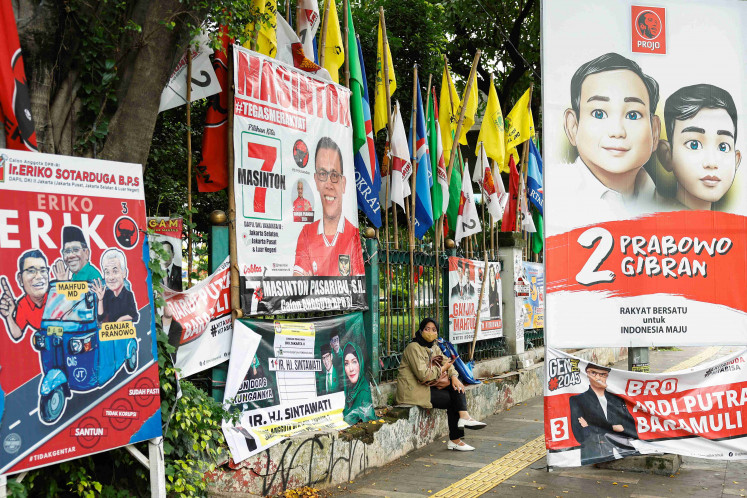A woman sits near flags and posters promoting the presidential and legislative candidates for the upcoming general election, in Jakarta, February 6, 2024. 
